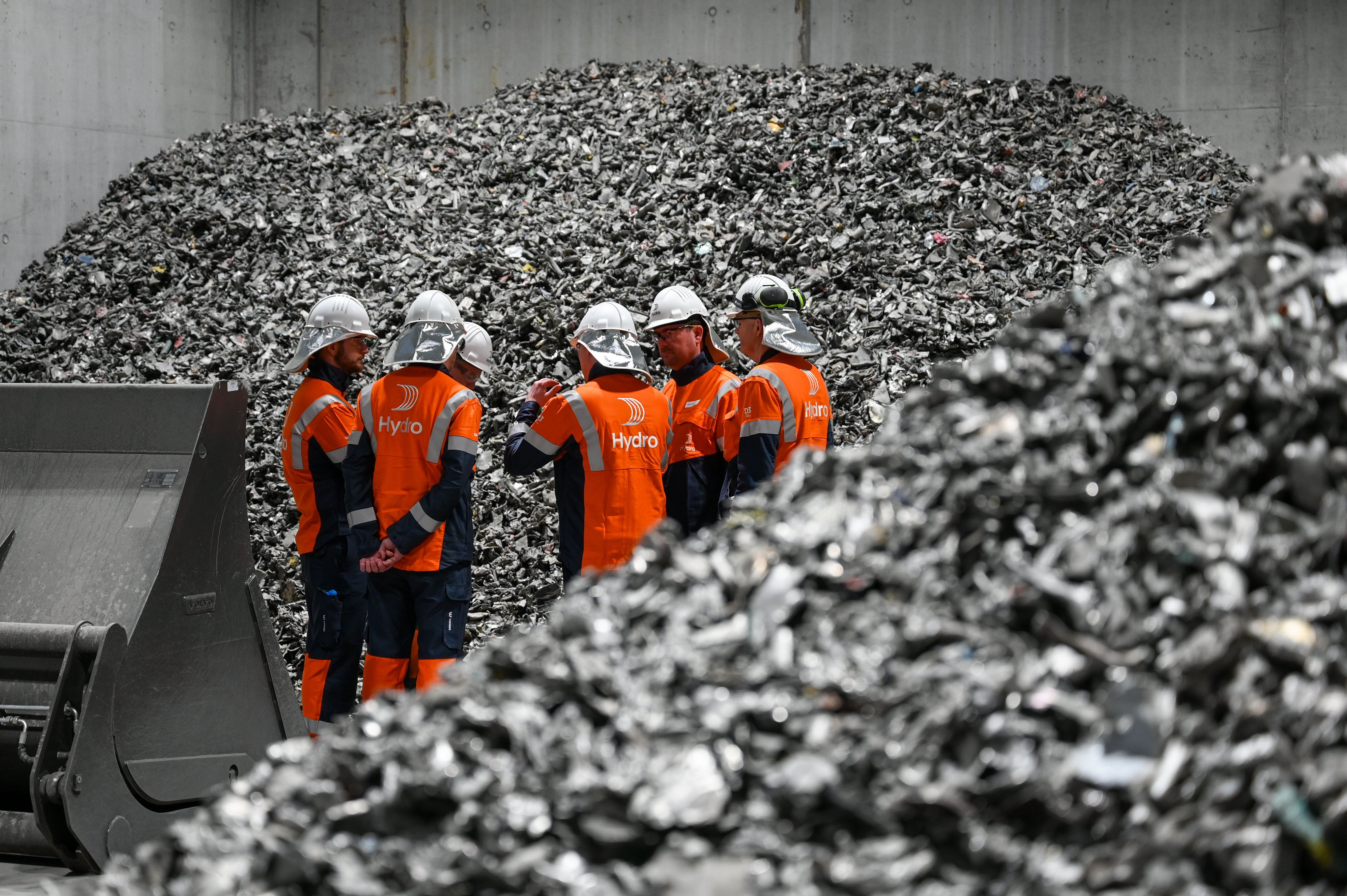 a group of men in orange uniforms and white helmets standing in front of a pile of garbage